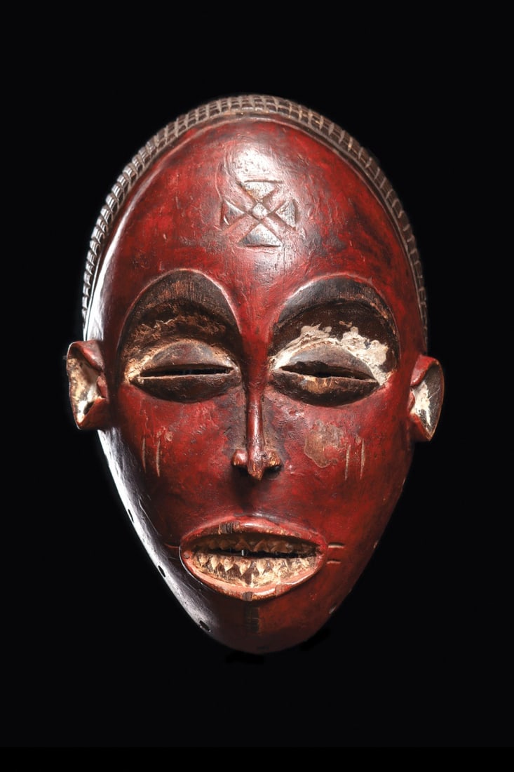 Chokwe Red-Face Mask: Angola. Mwana Pwo female mask with a tight grid-patterned coiffure and high domed forehead with relief cross motif. Refined features include recessed slit eyes with bulging lids, a narrow nose, and