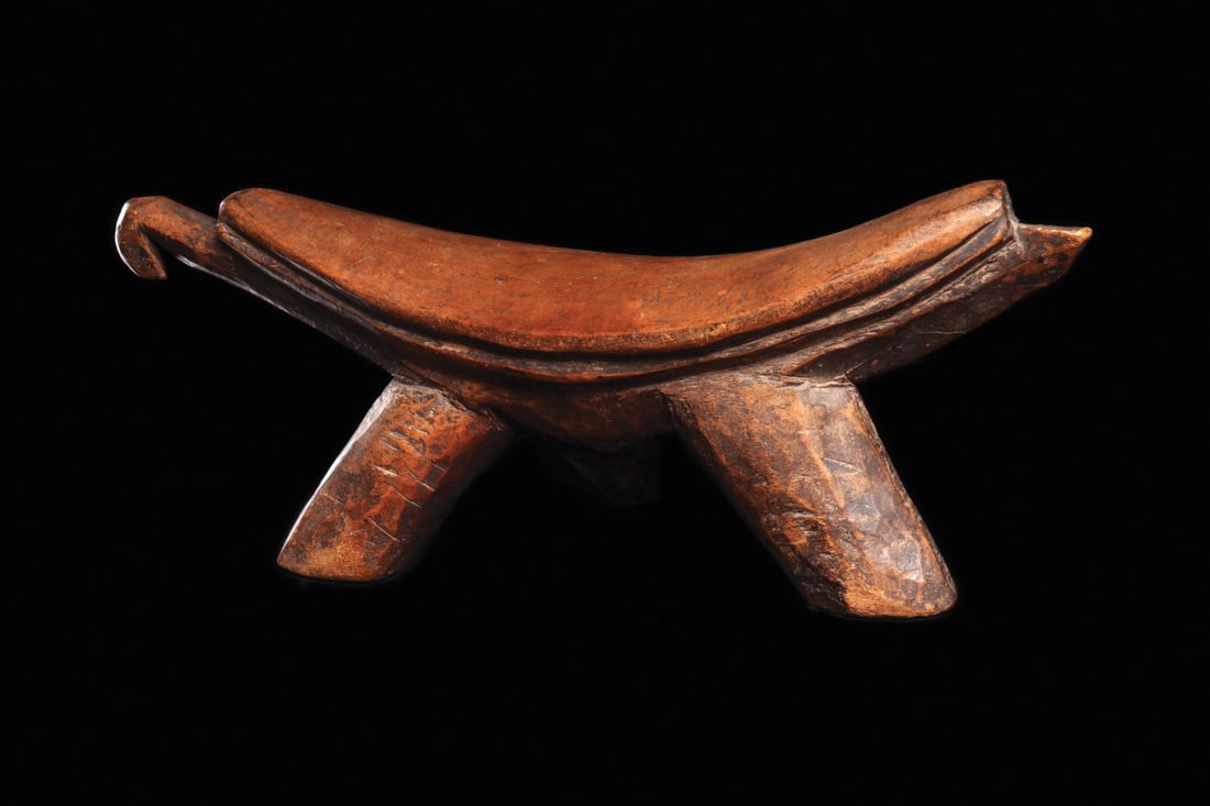 Dinka Headrest: South Sudan. Abstract tripod support carved from single piece of wood, with an avian head on one side. Used by nomadic herdsmen as pillow or seat. Variegated medium brown patina. 6" H × 17.25" L
