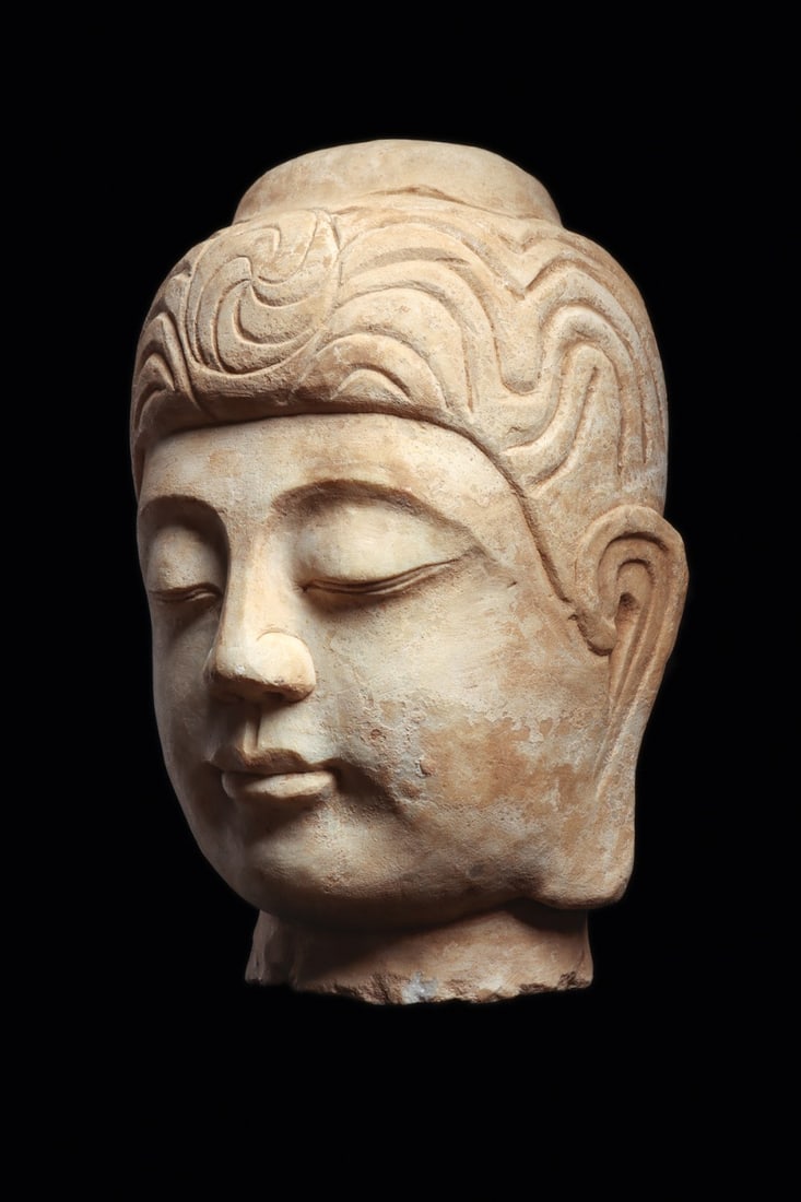 Ming Style Marble Buddha Head: China, 20th century. Decorative, carved white marble head of a Buddha having hair tied in neat wavy rows terminating in a low usnisa atop. Serene facial detail with heavy lids, small but full lips and