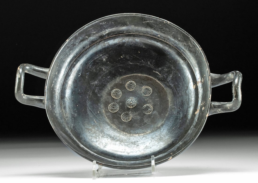 Lustrous Attic Kylix with Stamped Floral Motifs: Greece, Athens, ca. 525 - 475 BCE. Truly a work of art! A gorgeous ceramic kylix with a perfectly round, deep bowl that stands on a circular foot, and twin, delicate handles projecting from the sides,