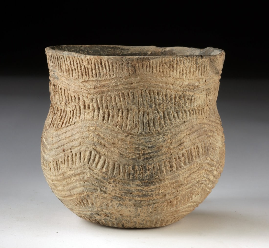 Mississippian Pottery Jar - Incised Wave Motif: Native American, Mississippian culture, ca. 800 to 1600 CE. A pottery jar of rounded form with a slightly everted rim, its surface richly textured with rhythmic incised bands and undulating wave motif