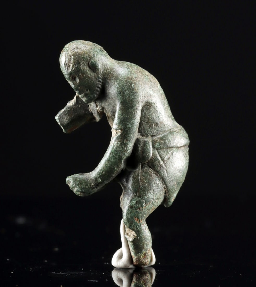 Greek Bronze Wrestler Relief Applique: Greece, Classical period, ca. 5th century CE. An enticing leaded bronze relief of a wrestler, depicted bald and bearded as he bends one leg, extending the others in defense. A short kilt is tied at hi