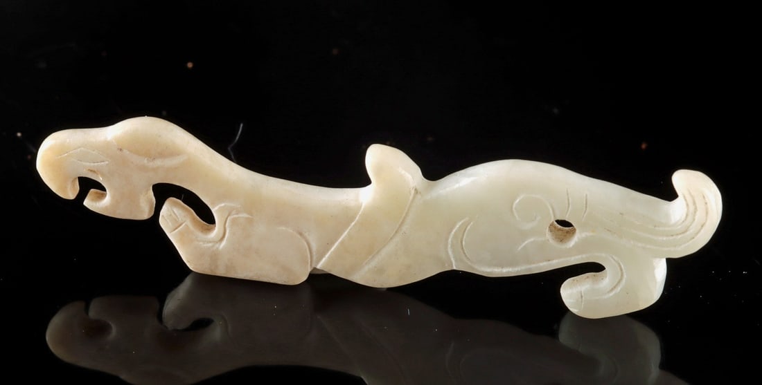 Chinese White Jade Pixiu Charm With Piercing: East Asia, China, ca. 20th century CE. A petite white jade carving depicting a sinuous zoomorphic form, perhaps a stylized feline or mythical pixiu beast with a hole for suspension. The stone is softl