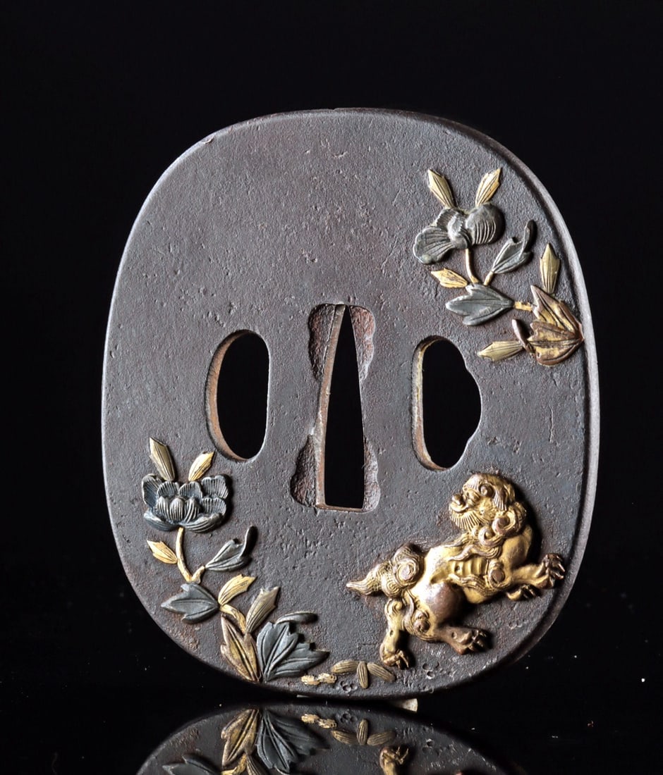 Japanese Edo Iron Tsuba, Gilt Flowers & Lion-Dog Motif: East Asia, Japan, Edo to early Meiji era, ca. 19th century CE. An iron tsuba sword guard of rounded rectangular form, decorated in relief with gilt and silver-washed motifs of flowering plants and a l