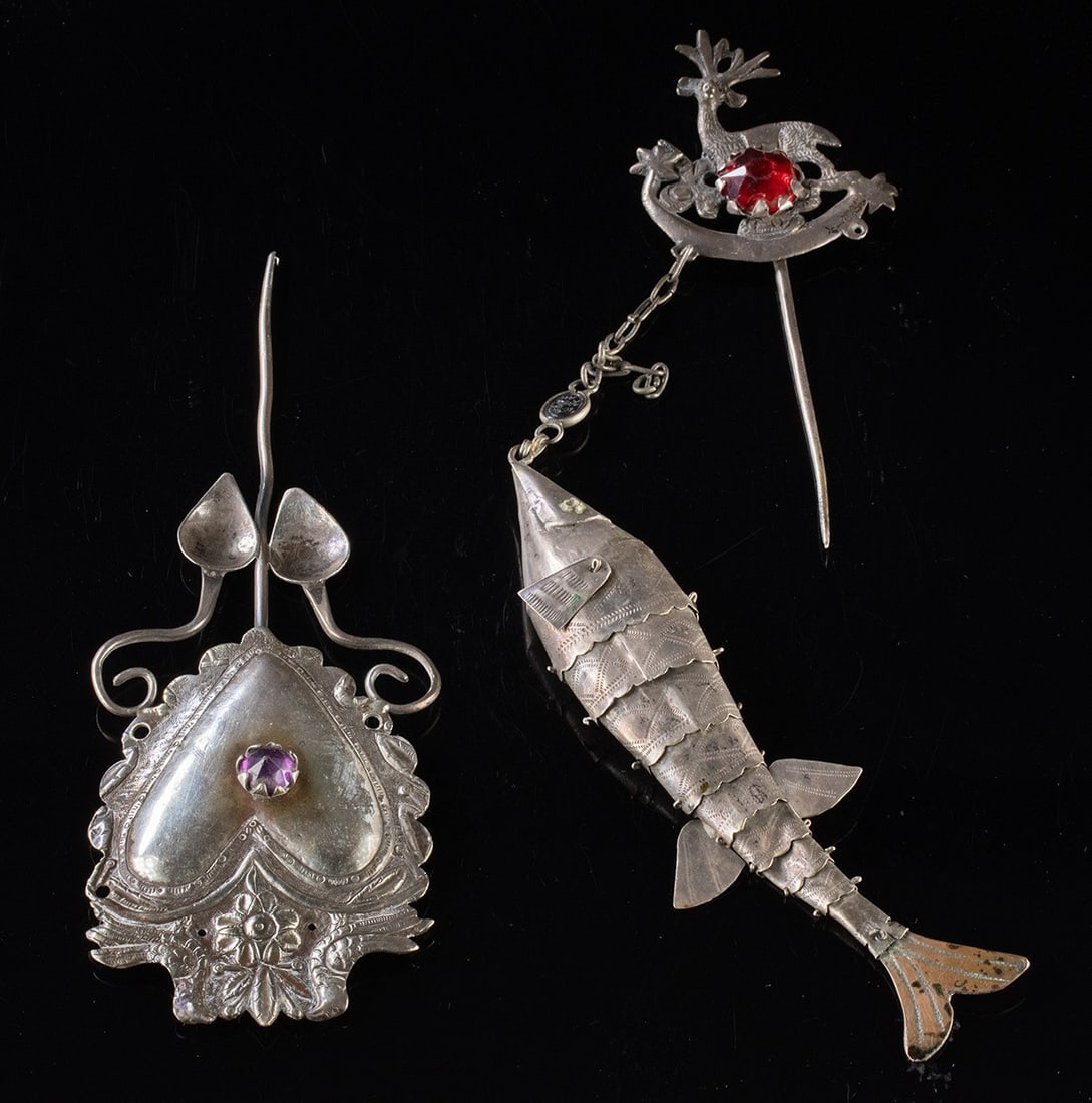 Two Andean Silver Tupu Pins, Heart Shaped & Fish Charm: South America, Peru / Bolivia, ca. early 20th century CE. A group of two silver tupu pins composed of mixed silver alloys and brass elements. One features a deer standing within a crescent form sugges