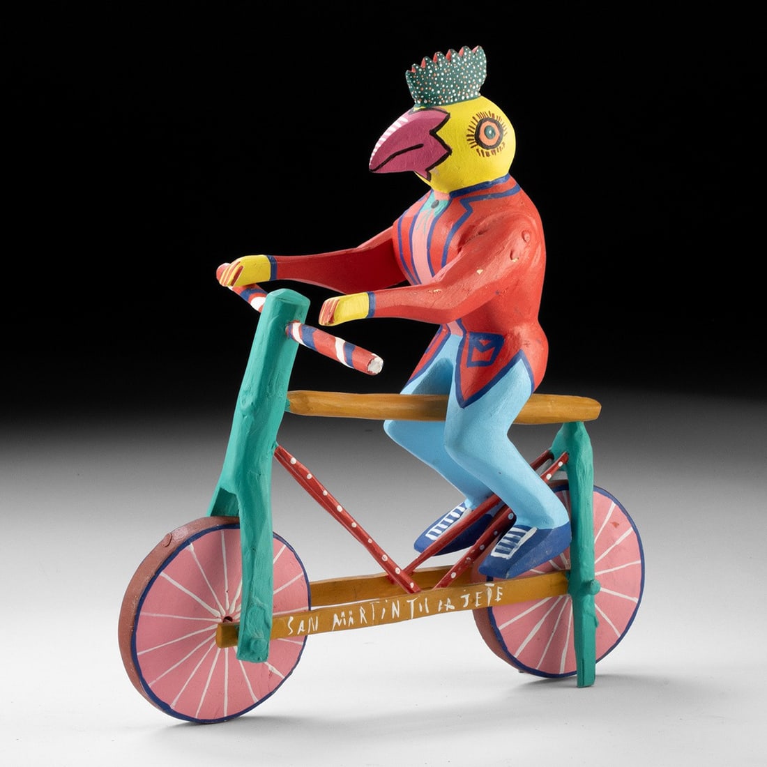 Mexican Folk Art Carved Wood Alebrije - Rooster on a Bicycle by Martin Melchor: Mexico, Oaxaca, San Martin Tilcajete, ca. late 20th to 21st century CE. A rooster riding a bicycle, carved in wood and painted in vibrant polychrome. The figure wears a dotted crest and dapper clothin