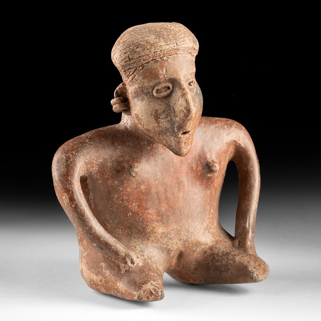 Jalisco Redware Seated Nude Female Figure - Incised Coiffure: Pre-Columbian, Mexico, Jalisco, ca. 300 BCE – 300 CE. A seated female figure modeled in burnished redware, her broad body reduced to essentials yet unmistakably alive. The long ovoid head, frame