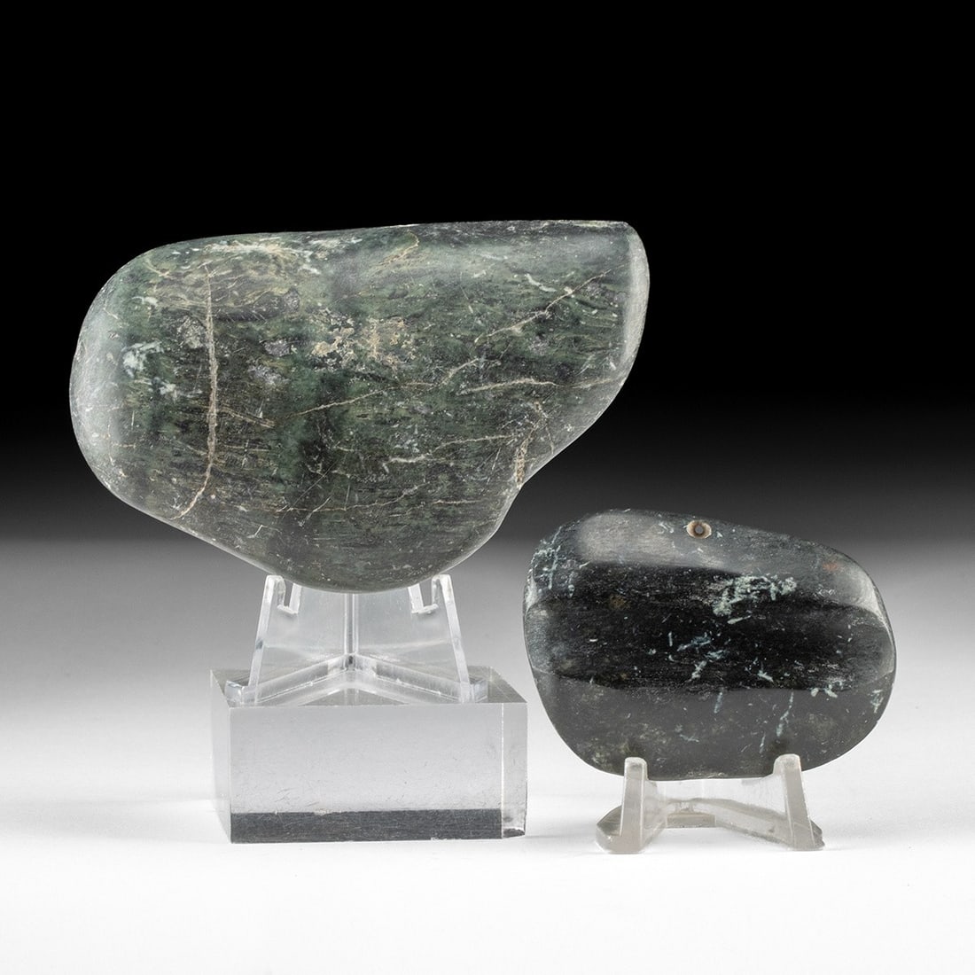 Two Costa Rican Greenstone Celt Pendants: Pre-Columbian, Costa Rica, ca. 300–800 CE. Pair of hand-polished greenstone pendants, worked to a soft, waxy luster along undulating contours. The larger stone shows a deep mottled green veined 