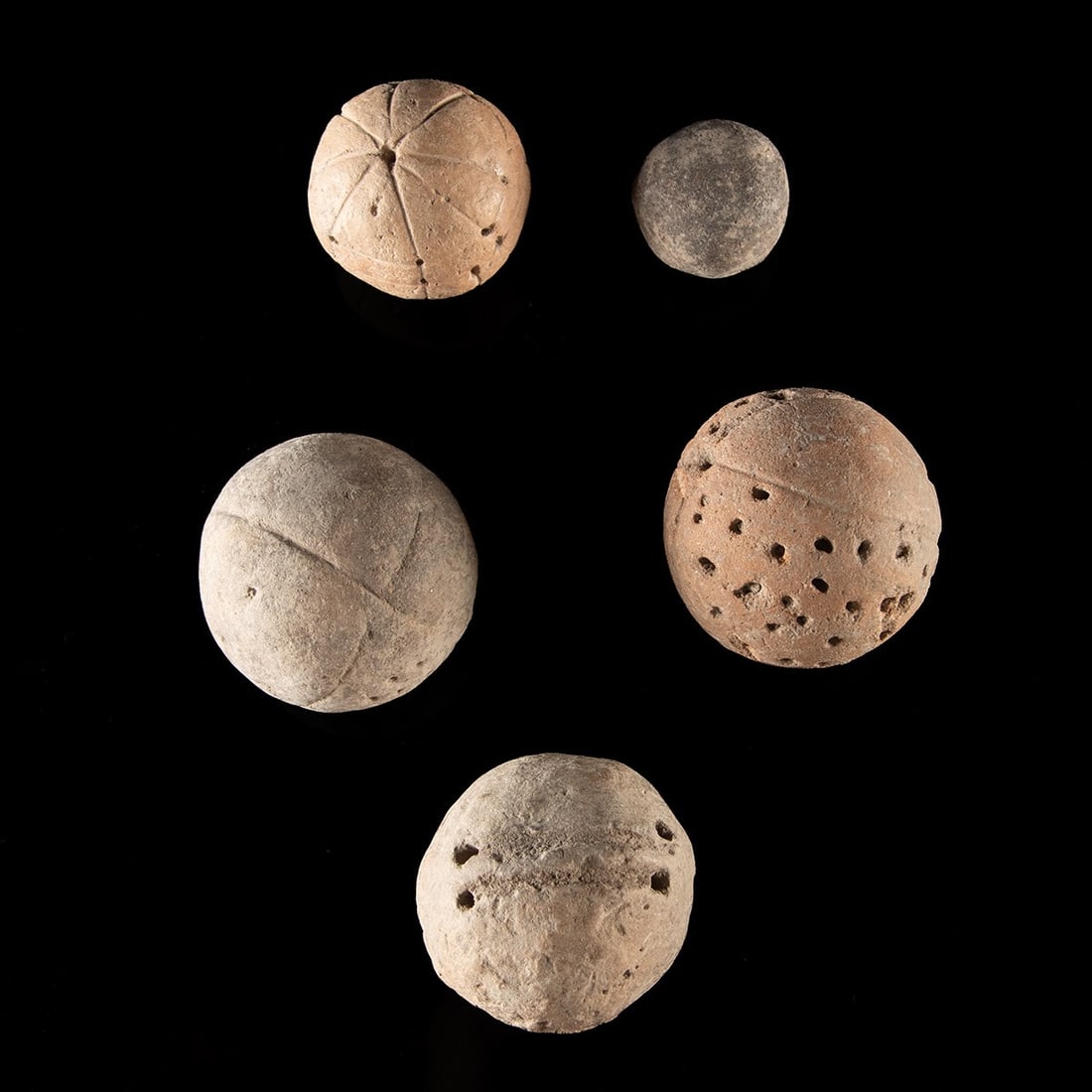 Mesoamerican Pottery Spheres, Group of Five - Pierced Vents and Incised Lines: Pre-Columbian, Mesoamerica, ca. 300 BCE – 1500 CE. A collection of five hollow pottery spheres, likely Pre-Columbian, possibly used as game pieces or rattles. The largest examples are pierced wi