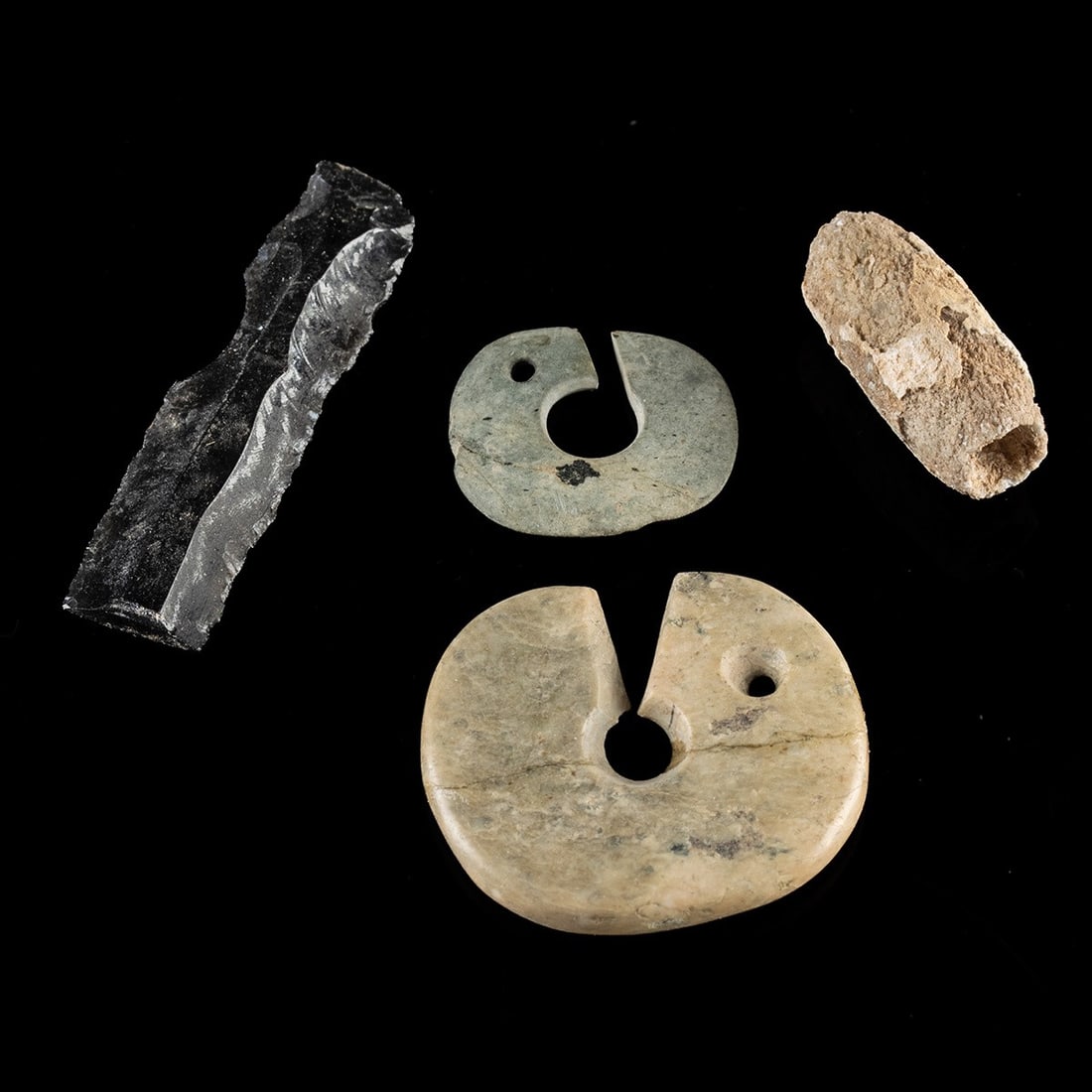 Ancient Stone Beads, Slit Discs & Knapped Obsidian Blade - Group of Four: Pre-Columbian, Mesoamerica & Asia, ca. 1000 BCE – 1500 CE. A group of four worked stone objects. The group includes an elongated obsidian blade flaked from a prepared core with sharp edges intac
