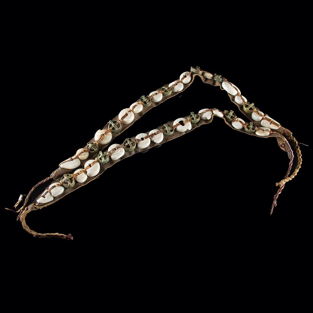West African Mali Leather Adornment Straps - Conus Shell Discs & Brass Discs: West Africa, Mali, ca. mid-20th century CE. A pair of leather straps from Mali or the wider West African region, each mounted along its length with alternating white conus-shell discs and cast brass o