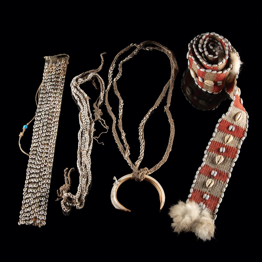 Papua New Guinea Fiber Adornments - Cowrie Shell & Boar Tusk: Melanesia, Papua New Guinea, ca. mid-20th century CE. A group of four woven fiber adornments from Papua New Guinea. The longest is a woven sash band using nylon cords in red and white edged with seed 