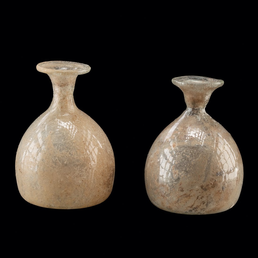 2nd C. Roman Glass Miniature Unguentaria, Pair - Iridescent Bulbous Flasks: Roman, Imperial period, ca. 100–300 CE. A pair of Roman glass miniature unguentaria vessels. Each is free blown of pale green and translucent glass with a globular body rising to a constricted n