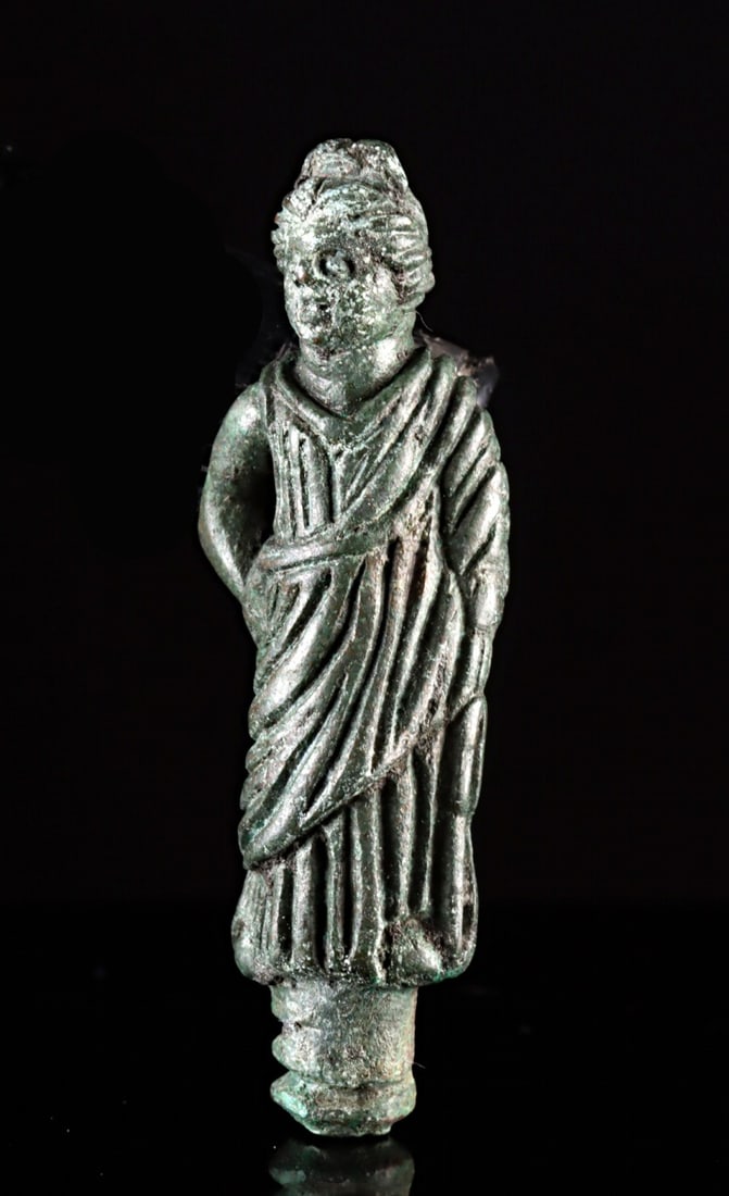 Roman Leaded Bronze Votive of a Woman: Roman, Imperial period, ca. 1st to 3rd century CE. A delightful leaded bronze votive figure of a woman, perhaps a goddess, standing with one hand on her hip and the other at her side. Billowing folds 