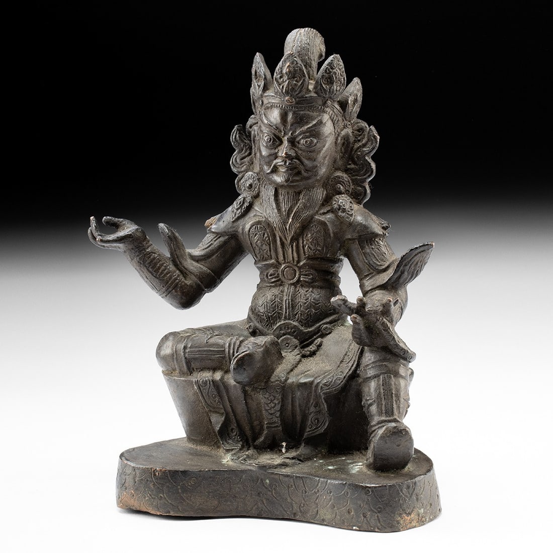 18th C. Tibetan Copper Deity - Armored Guardian with Serpent: East Asia, Tibet, ca. 1700–1900 CE. A commanding cast-copper figure of a wrathful deity, seated in a relaxed half-lotus with one leg folded and the other pendant, resting upon a lobed lotiform b