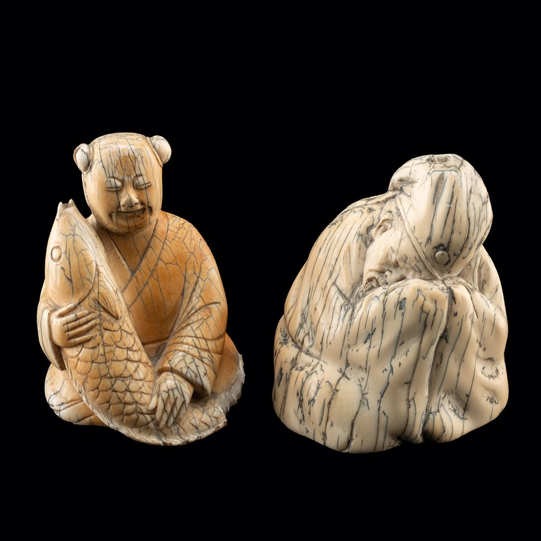 Two Mammoth Ivory Okimono, Sleeping Man and Figure with Fish: East Asia, China / Japan, ca. early to mid-20th century CE. A pair of okimono figures carved from mammoth ivory. The first depicts a seated figure with hair dressed in twin buns, cradling a large fish