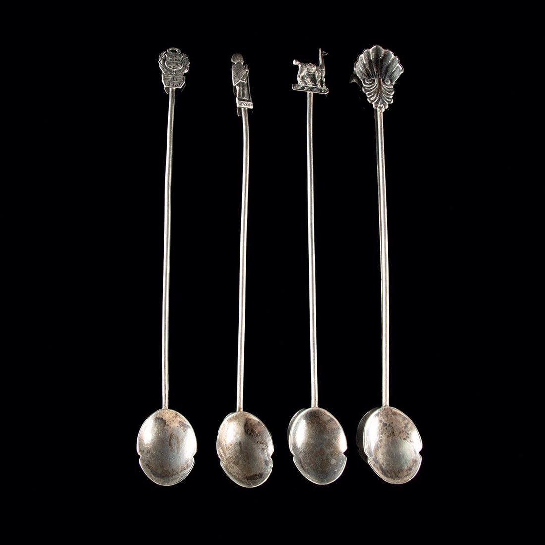 20th C. Peruvian Silver Souvenir Spoons - Coat of Arms, Llama & Shell, Set of 4: South America, Peru, ca. 1900–1999 CE. A quartet of slender silver spoons, their long tapering handles rising to figural finials that celebrate Peruvian identity. One is crowned by the national 