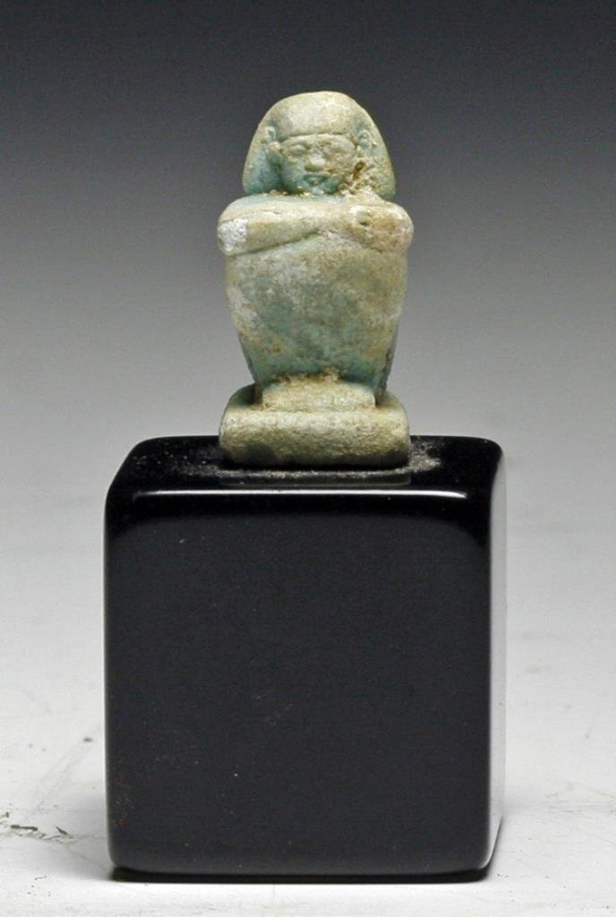 Miniature Egyptian Faience Seated Scribe: Starts at $100 Egypt, ca. 26th Dynasty, 7th - 6th Century BCE. Light blue faience figure of a seated scribe with arms crossed. Fine detail of face. Custom mount. Scribe measures 1"H. Provenance: Ex-Pr