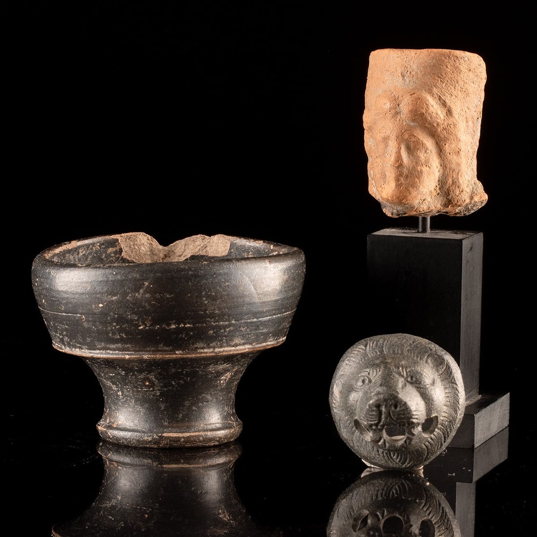 Greco-Roman Terracotta Female Head, Blackware Cup, Bronze Lion Head: Western Greece, Archaic Period & Magna Graecia / Roman Empire, ca. 600 BCE – 300 CE. A small collection of three ancient objects from classical antiquity, including a mold-made terracotta female