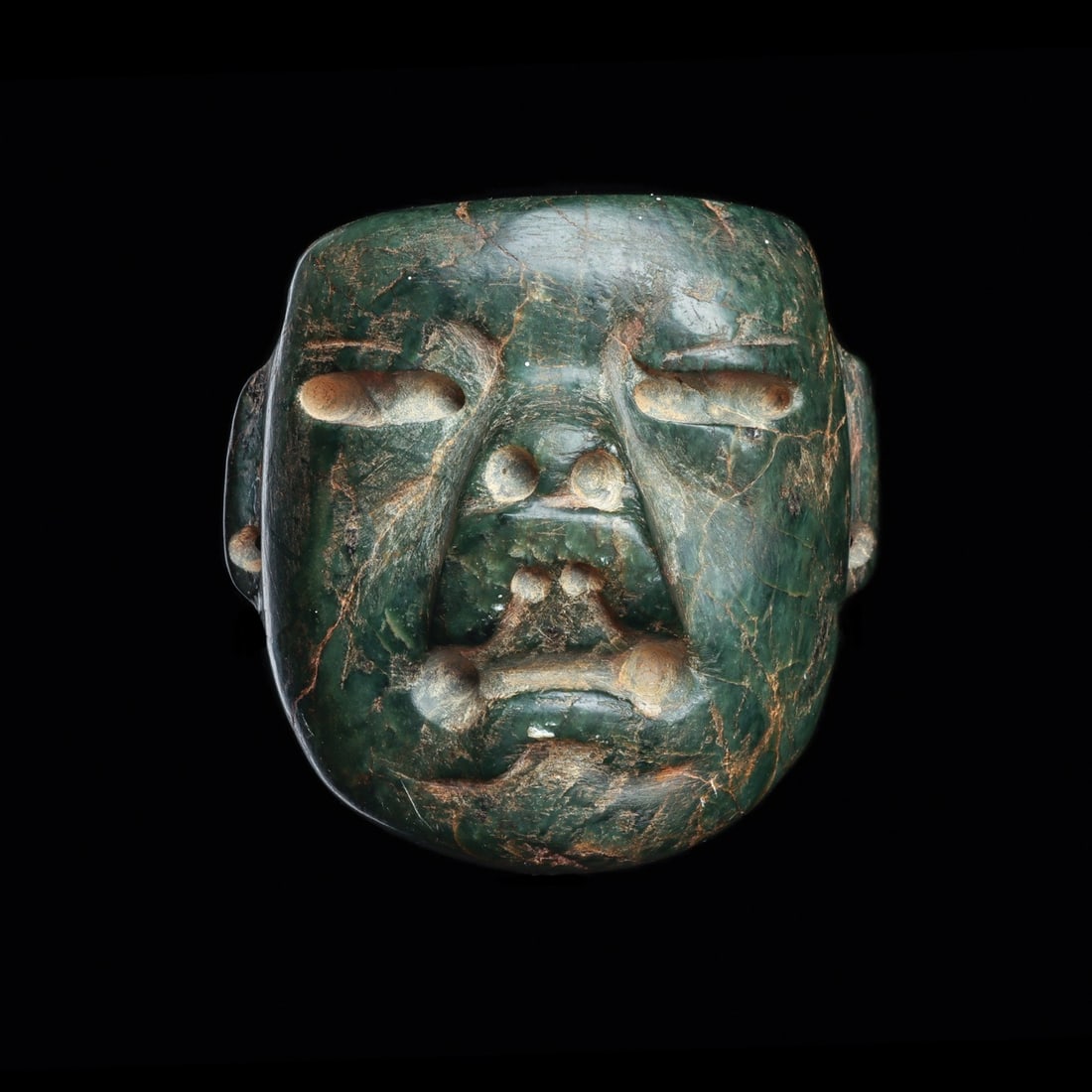 Olmec Serpentine Maskette Pendant, Jaguar Transformation Face: Pre-Columbian, Mexico, Olmec, ca. 1000–600 BCE. A small mask of deep green serpentine, carved as a human face caught mid-transformation into a jaguar. Slit eyes are drilled and recessed beneath 