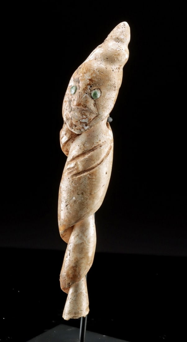 Colima Conch Shell Pendant with Jade Eyes: Ca. 300 BCE – 300 CE. Pre-Columbian, West Mexico, Colima culture, ca. 300 BCE to 300 CE. A pendant carved from the spire of a conch shell into an abstract anthropomorphic figure. The natural cur
