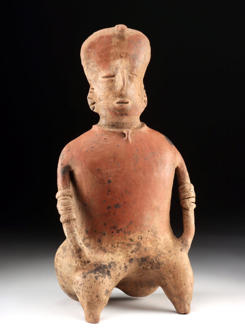 Nayarit Seated Figure with Shaman's Horn: Pre-Columbian, West Mexico, Nayarit, ca. 300 BCE – 300 CE. A pottery figure shown seated with hands resting on thighs. Facing forward, the elongated head features slit-form eyes, a pinched nose,
