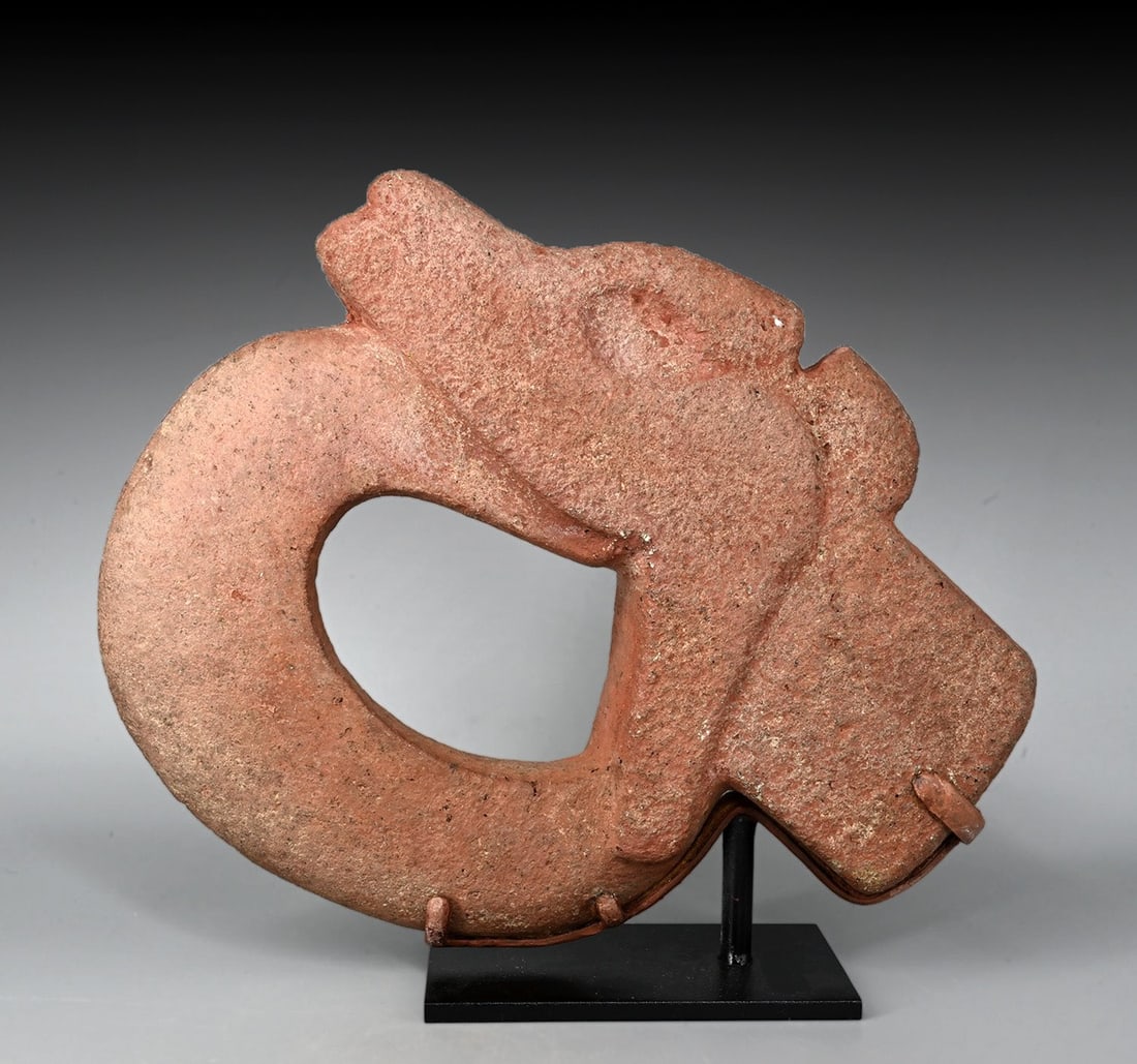 Veracruz Openwork Stone Hacha, Jaguar Head: Pre-Columbian, Mexico, Veracruz, ca. 600–900 CE. A gray volcanic stone hacha, its surface saturated with red cinnabar, carved as an abstract jaguar head seen in profile. The wide open jaws frame