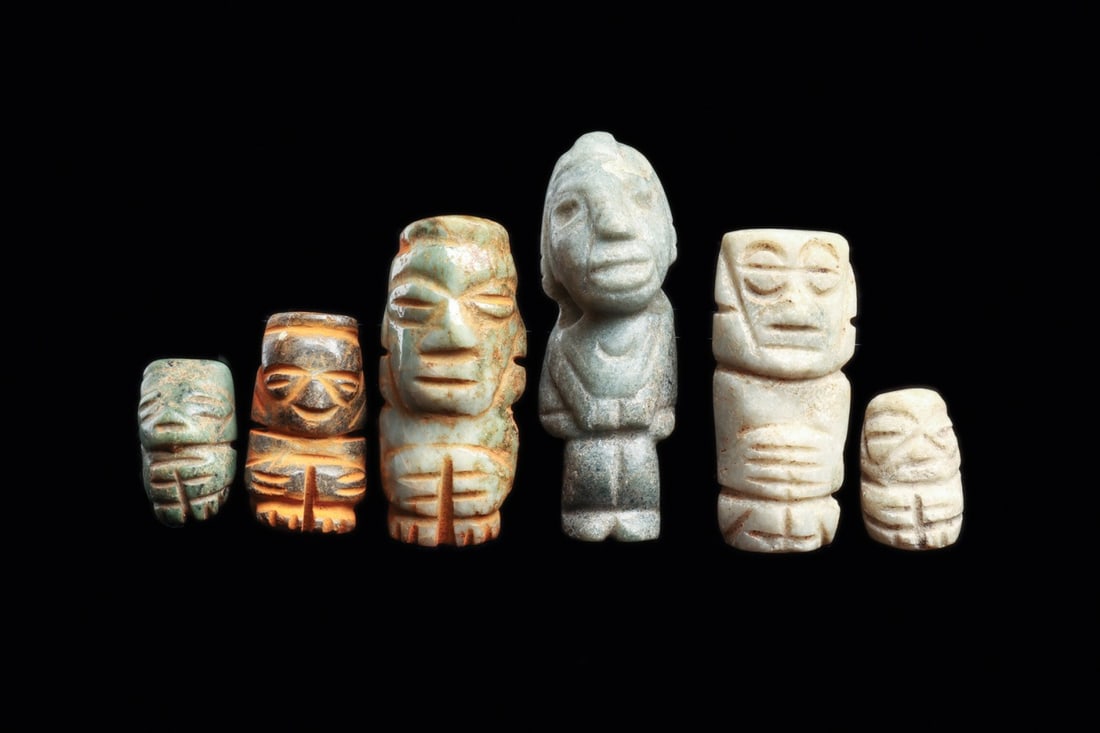 Mixtec Penate Amulet Group of Six, Miniature Carved Stone Pendants: Pre-Columbian, Mexico, Oaxaca, Mixtec, ca. 800–1200 CE. A group of six miniature standing figures carved from jadeite and serpentine in pale green, white, and mottled russet stone. Each is reduc