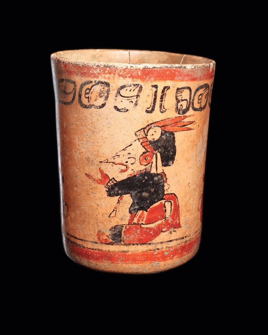 Maya Polychrome Cylinder Vase with Long-Nosed Speaking Lords and Glyph Band: Pre-Columbian, Mesoamerica, Maya, ca. 500–800 CE. A cylinder vase painted in red and black on a cream-buff slip, its walls carrying two seated lords in mirrored composition. Each wears a feather