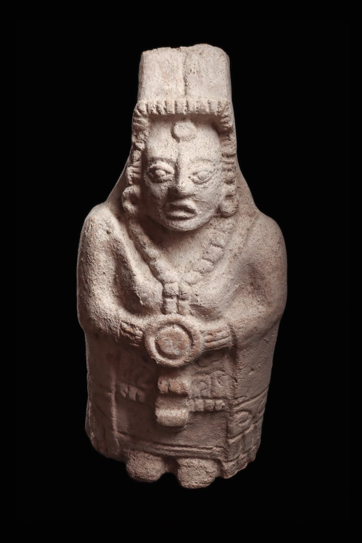Maya Large Hollow Mold-Made Dignitary Figure with Shield: Pre-Columbian, Mexico, Maya, ca. 500–800 CE. A hollow, mold-made pottery dignitary stands frontally in a floor-length hooded robe, both hands closed over a small circular shield worn at the ches