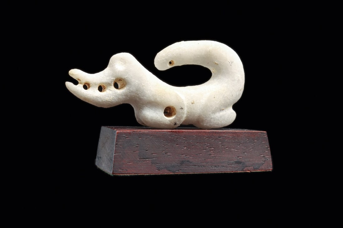 Costa Rican Quartzite Crocodile Pendant with Curled Tail: Pre-Columbian, Costa Rica, ca. 500–1000 CE. A miniature crocodilian carved from semi-translucent white quartzite, its long tail sweeping up and curling over the back to enclose a crisp lunette o