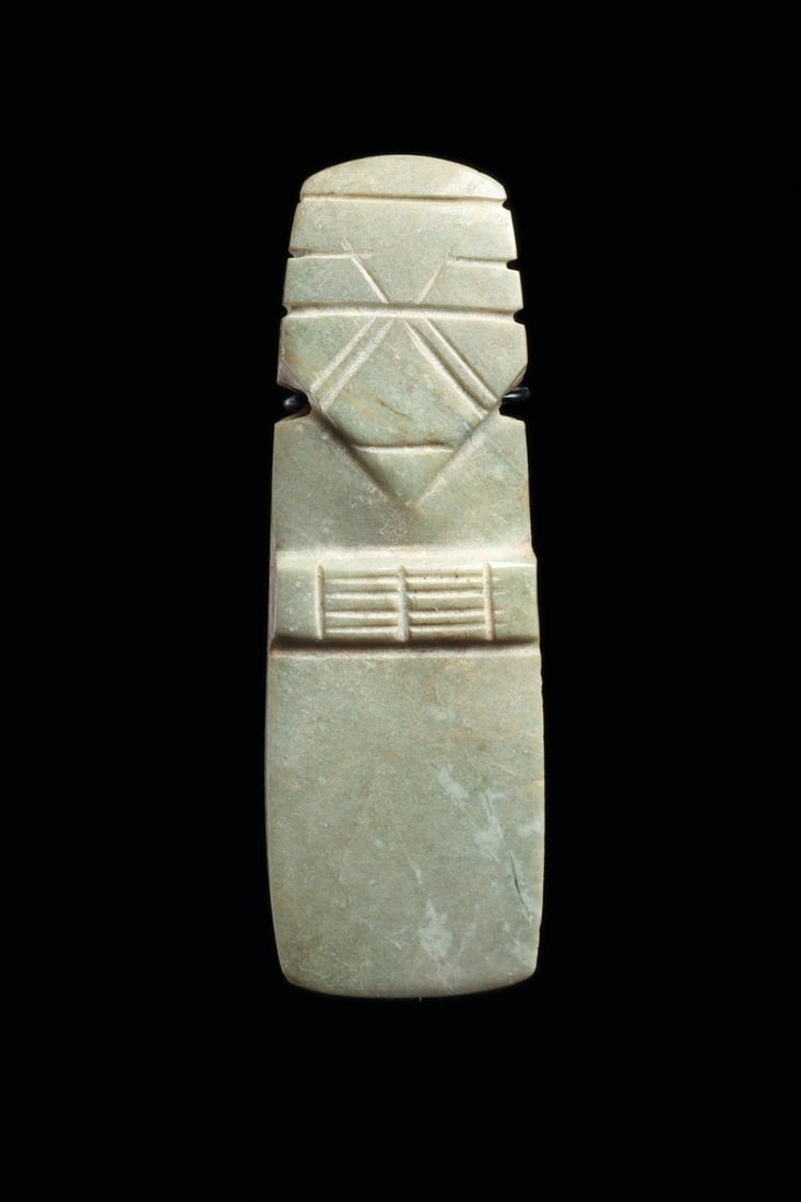 Costa Rican Jade Axe-God Celt Pendant with Incised Face: Pre-Columbian, Costa Rica, ca. 500–1000 CE. A standing figure distilled into the blade of a celt, carved from grayish blue-green jade with a softly lustrous polish. The upper third bears the hea