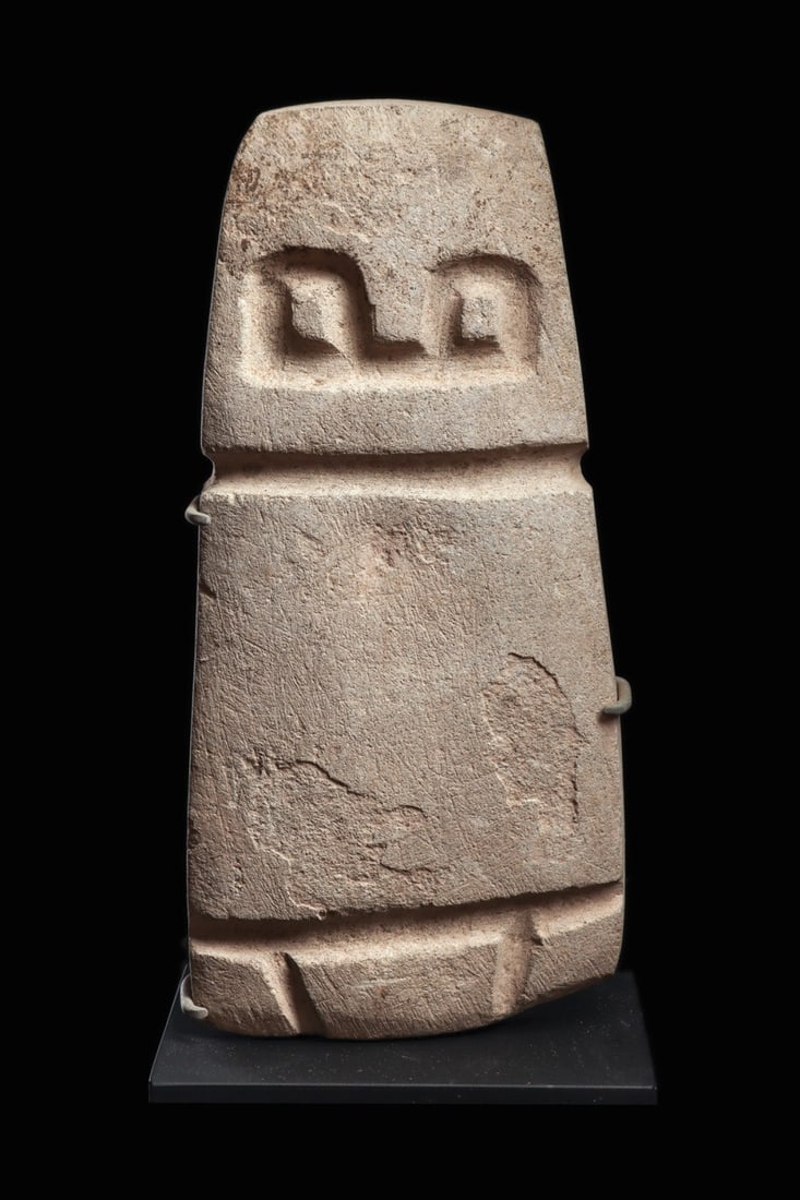 Valdivia Stone Slab Figure with Recessed Eyes: Pre-Columbian, Ecuador, Valdivia, ca. 2300–2000 BCE. A columnar figure reduced to its essentials, carved from compacted limestone into a flat, tapering slab. The rounded head carries a pair of d