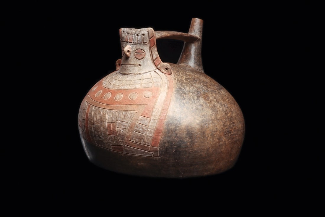 Paracas Chocolate Ware Deity Head Bridge-Spout Vessel: Pre-Columbian, Peru, South Coast, Paracas culture, ca. 500–200 BCE. A squat, globular chocolate ware jar crowned by a modeled deity head, its features cut in crisp incision: slit eyes, a project