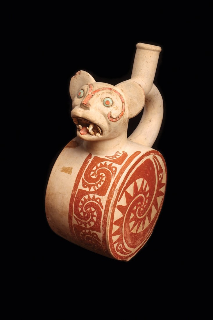 Moche Jaguar Stirrup Vessel with Shell and Turquoise Inlay: Pre-Columbian, Peru, Moche, ca. 100–300 CE. A snarling feline rears from the shoulder of this drum-bodied bottle, modeled in buff ceramic and finished in red-brown slip on cream. The jaguar's br