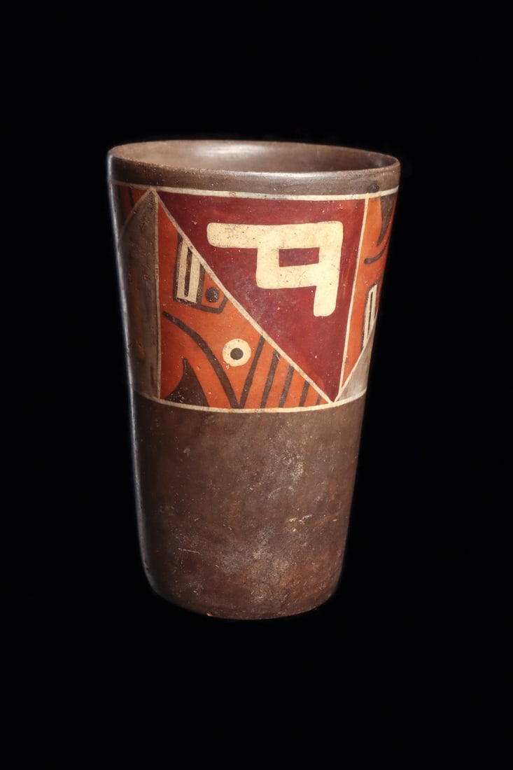 Tiwanaku Polychrome Kero with Geometric Half-Faces: Pre-Columbian, Bolivia, Tiwanaku, ca. 700–1000 CE. A flaring ceramic beaker of classic kero form, its tapered walls rising from a narrow base to a wide drinking rim. The lower body is left a bur