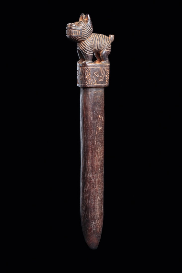 Wari Wood Baton with Standing Dog Finial: Pre-Columbian, Peru, Wari, ca. 650–900 CE. A hardwood baton crowned by a small carved dog, its ridged coat rendered in tight parallel grooves, ears perked, muzzle bared to show a full row of tee
