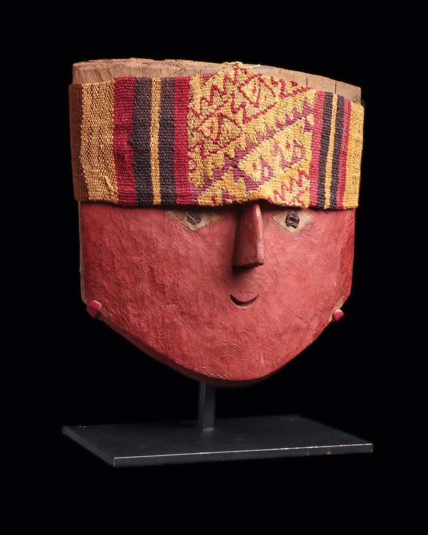 Chancay Wooden Mummy Mask with Textile Headband, Red Cinnabar Pigment: Pre-Columbian, Peru, Central Coast, Chancay, ca. 1000–1250 CE. A broad shield-shaped face carved from a single plank of light wood, its surface saturated with red cinnabar pigment. Lozenge-shape