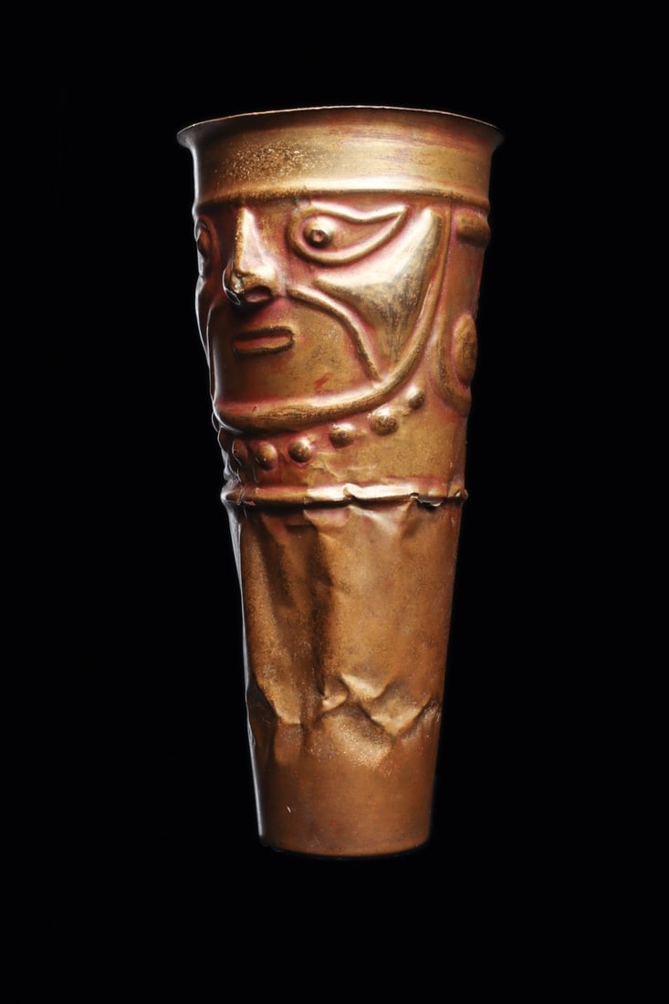 Chimu Lambayeque Anthropomorphic Beaker with Dignitary Head, Peru: Pre-Columbian, Peru, North Coast, Chimu / Lambayeque, ca. 1000–1250 CE. A tapered cylindrical beaker raised from sheet copper, its upper register worked in high repousse relief into the face of 