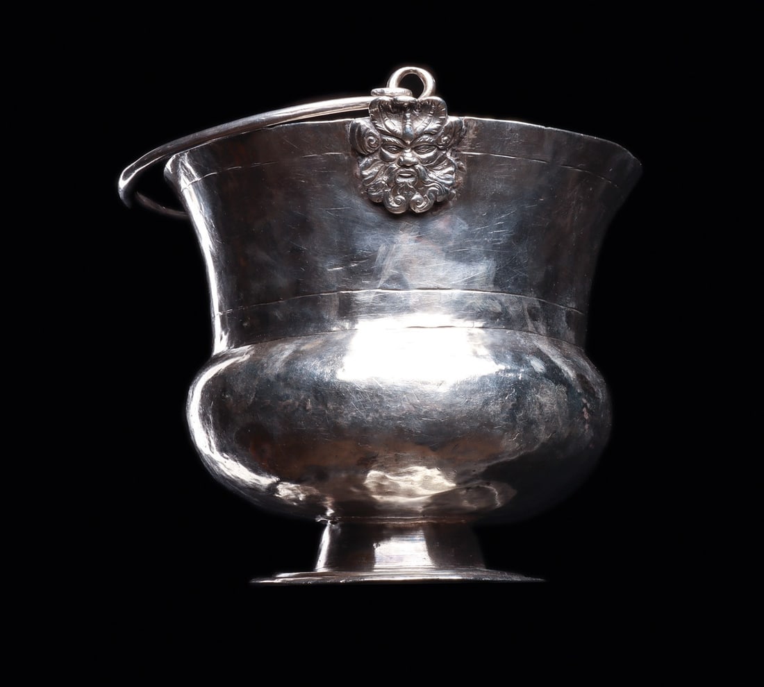 Spanish Colonial Acetre Holy Water Bucket with Devil of Puno Masks, 18th C.: South America, Bolivia, Lake Titicaca region, Spanish Colonial, 1750 CE. A heavy hammered silver acetre, the vessel from which a priest carried holy water for aspersion. The wide flaring upper wall dr
