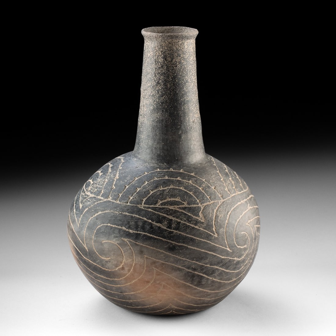 Caddo Engraved Blackware Bottle | Trans Mississippi South: Native American, Caddo, ca. 1200–1500 CE. A globular bottle with a tall, flaring neck, the burnished blackware body carrying engraved scroll and spiral decoration. Sweeping scrolls and interlock