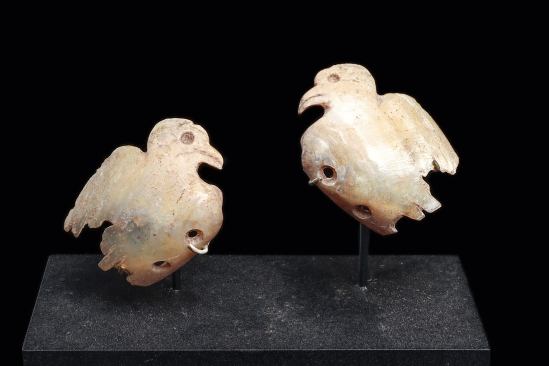 Mississippian Mother of Pearl Bird Pendants, Miniature Pair: Native American, Mississippian culture, ca. 1450–900 BCE. A matched pair of miniature raptors cut from marine shell, each carved to follow the natural curve of the nacre so the bodies swell and 
