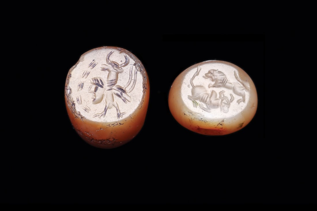 Sasanian Agate Stamp Seals with Lion and Bull-Headed Figure (2): Western Asia, Sasanian Empire, ca. 400–600 CE. A pair of domed agate stamp seals in warm amber and cream banding, each drilled longitudinally for suspension on a cord or wire. The flat faces car