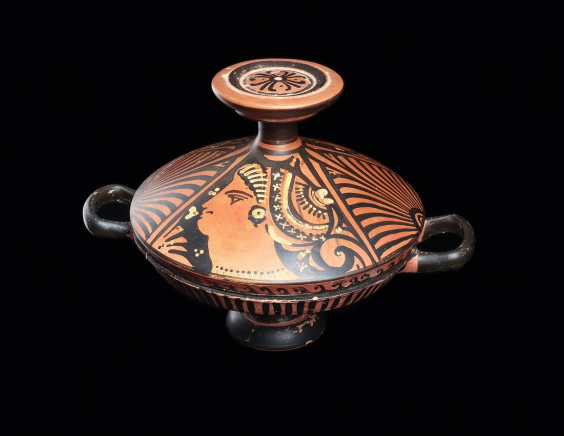 Apulian Red Figure Lekanis with Lady of Fashion Heads: Southern Italy, Apulia, Greek, 350 BCE. A lidded terracotta lekanis, its shallow bowl raised on a pedestal foot and fitted with two opposing loop handles. The domed lid carries two profile female head