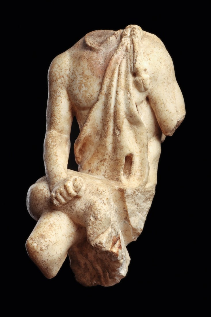 Roman Marble Seated Satyr Torso with Wineskin, 1st-2nd C. CE: Roman, Imperial period, Eastern Mediterranean, ca. 1–200 CE. A seated satyr carved in white marble, preserved from shoulders to knees, his athletic torso turning gently over crossed thighs. A ma