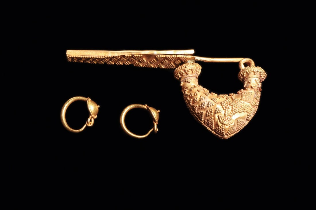 Magna Graecia Granulated Gold Bow Fibula with Child's Earrings, 5th C. BCE: Southern Italy, Magna Graecia, Greek colonial, ca. 500–400 BCE. A hollow gold bow fibula whose swelling arc is carpeted in granulation, minute spheres massed into diamonds, triangles, and zigzag