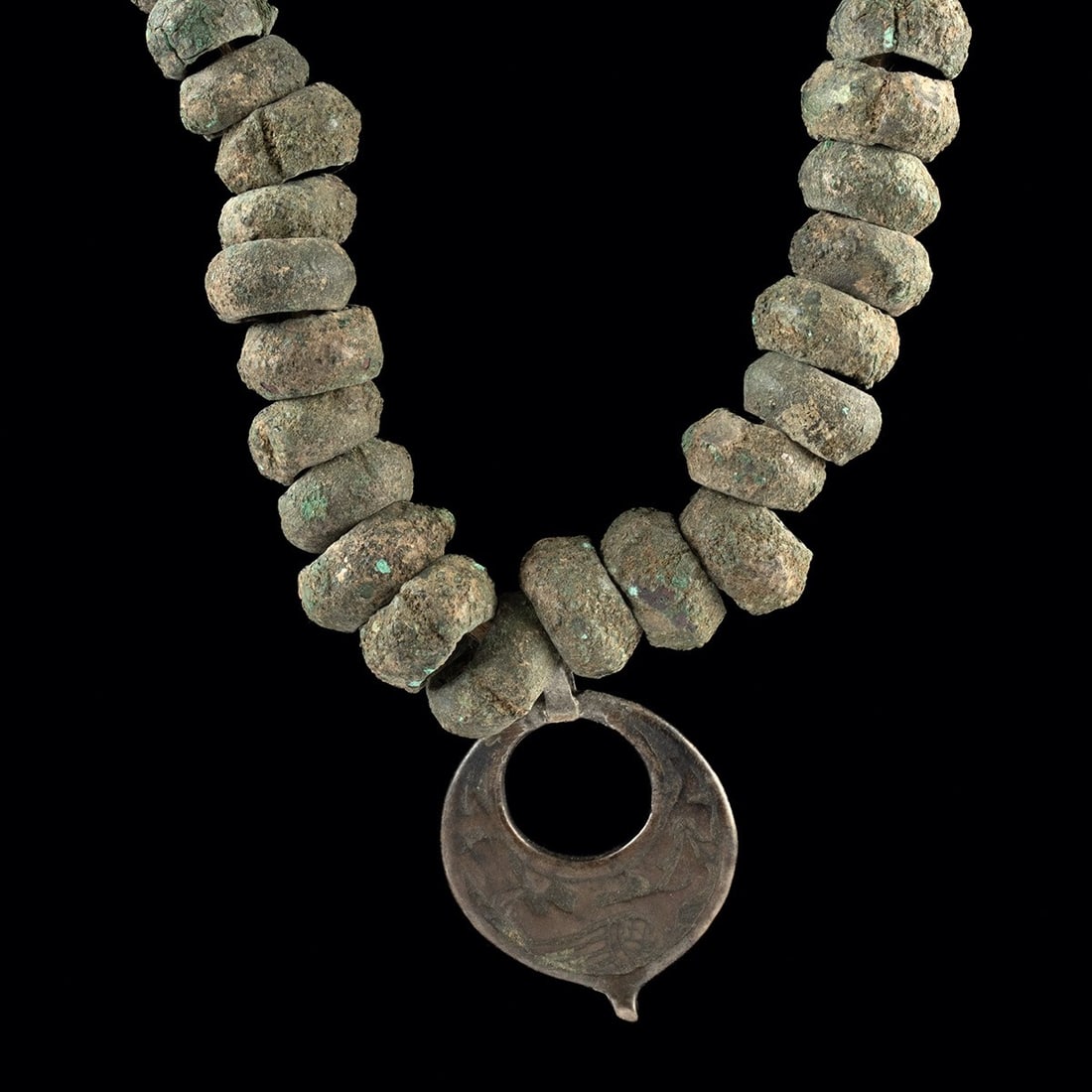 Luristan Bronze Bead Necklace with Seljuk Pendant: Western Asia, Iran, Luristan and Seljuk, ca. 1000 BCE – 1200 CE. A strand of graduated bronze beads, with a matte grey-green patina consistent with burial, gathered toward a small openwork penda