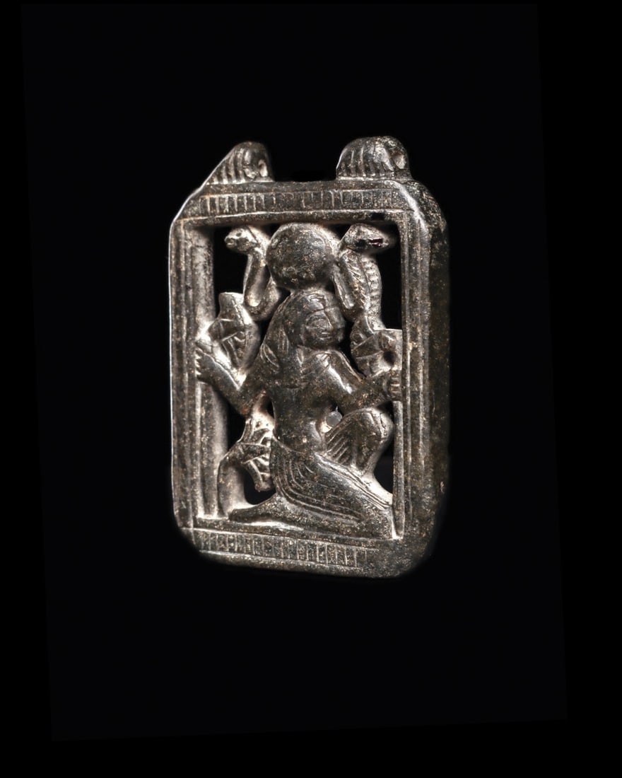 Egyptian Serpentine Openwork Pectoral Plaque with Hathor, Late Period: Egypt, Late Period, 600 BCE. A small pectoral plaque cut from black serpentine and pierced clean through, so the goddess sits inside her own window. Hathor kneels in profile, one arm raised, crowned w