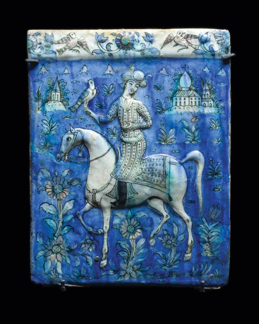 Persian Qajar Molded Tile with Falconer on a White Horse: Near East, Persia, Qajar period, ca. 1650–1850 CE. A young falconer rides out across a cobalt world in low relief, his hooded bird perched on a gloved fist raised against the sky. The molded ear