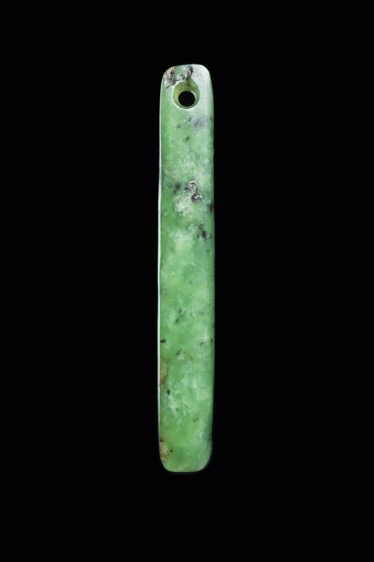 Maori Nephrite Kuru Ear Pendant, Contact Period: Oceania, New Zealand, Maori culture, ca. 1642–1840 CE. A slender tapered baton of deep green nephrite, drilled at the crown for suspension and polished to a soft matte sheen. The stone is kawaka